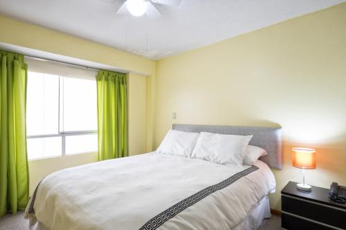 a bedroom with a bed with green curtains and a window at La Masia Apartments in Lima