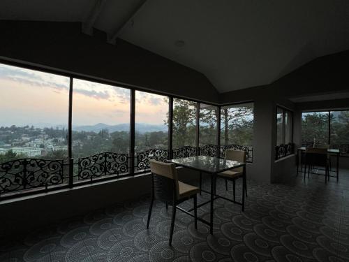 uma sala de jantar com mesa, cadeiras e janelas em Sunset Villa em Coonoor