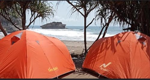 dos tiendas naranjas en la playa cerca del océano en Madasari Outdoor Camping Standar en Bulakbenda
