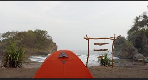 una tienda roja sentada en una playa junto al océano en Madasari Outdoor Camping Standar en Bulakbenda