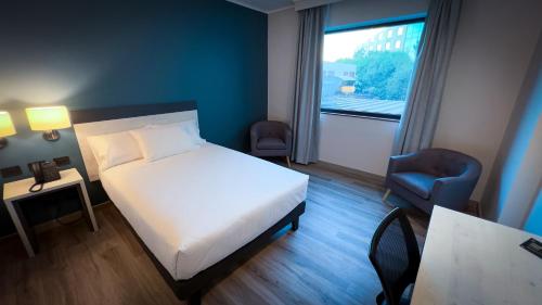 a bedroom with a bed and a chair and a window at Hotel Diego de Almagro Pudahuel Aeropuerto in Santiago