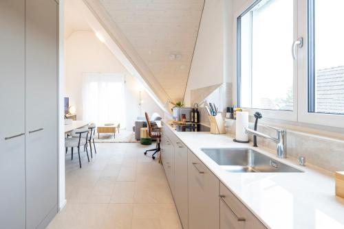 a white kitchen with a sink and a dining room at STAYY Flagship Limmattal - contactless check-in in Schlieren