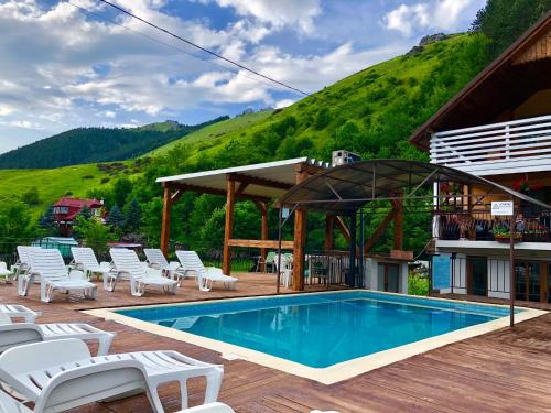 a swimming pool with white chairs and a mountain at Casa de vis Băișoara in Băişoara