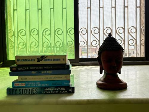 una pila de libros sentados en un estante con una estatua en Amma’s Om stay, en Patna