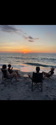 a group of people sitting on the beach watching the sunset at Kavvayi Kayaloram The Arabian Beach House in Kokkānisseri
