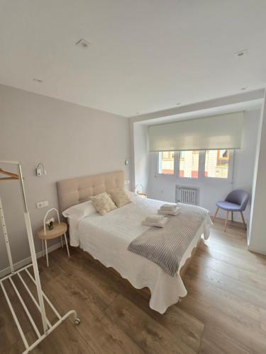 a white bedroom with a large bed and a chair at Piso en pleno Centro de Gijón al lado de la Playa in Gijón