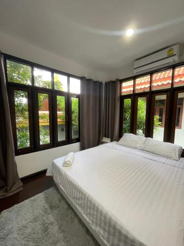 a bedroom with a large white bed with windows at Aisawan Resort villa in Surin Beach