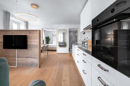 a kitchen with white cabinets and a flat screen tv at VISIMO Apartments Chur in Chur