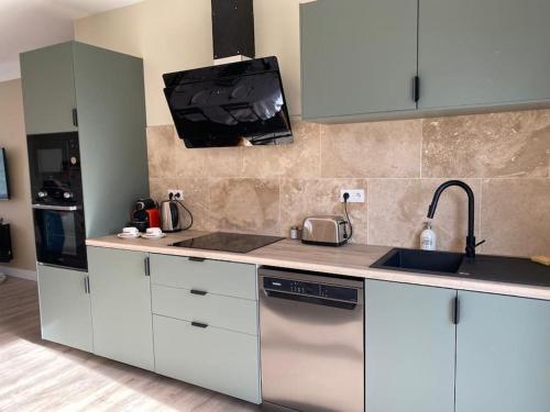 Il comprend une cuisine avec des placards blancs, un évier et une télévision. dans l'établissement Villa détente jacuzzi, à Saint-Étienne-de-Fougères