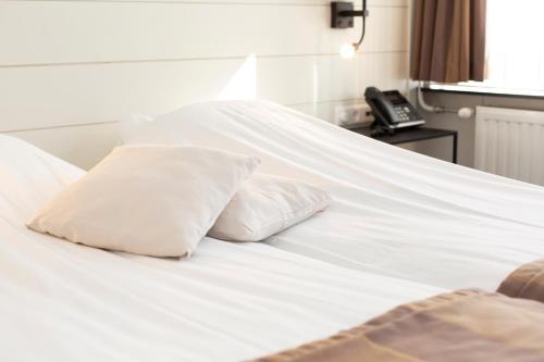 a white bed with two pillows and a phone at Restaurant-Hotel de Watergeus in Noorden