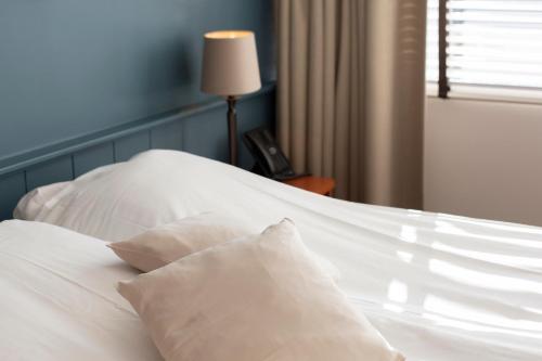 a white bed with white pillows and a lamp at Restaurant-Hotel de Watergeus in Noorden