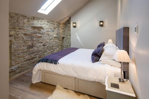 een slaapkamer met een groot bed en een stenen muur bij Williamston Cowshed in Slaggyford