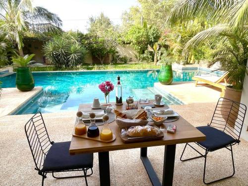 a table with food and a bottle of wine next to a pool at Villa YEMAYA - Villa d'hôtes in Ngaparou