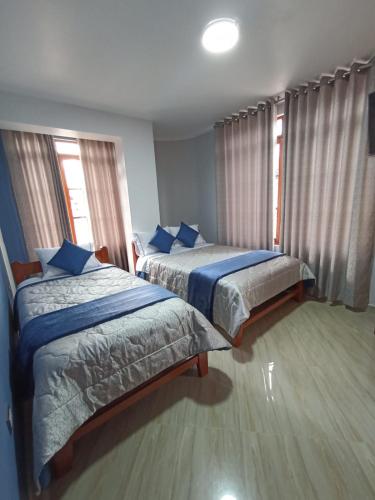 a bedroom with two beds with blue sheets and windows at HOSPEDAJE VALLE VERDE in Oxapampa