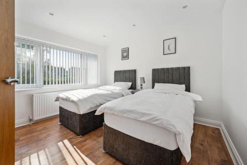 two beds in a bedroom with white walls and wood floors at house in Heald Green village in Manchester