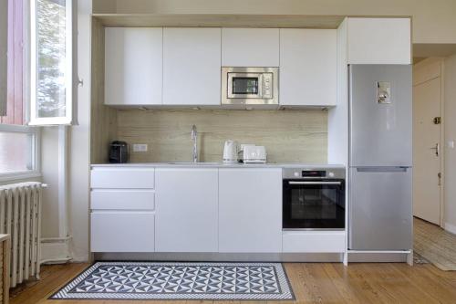 une cuisine blanche avec un évier et un micro-ondes dans l'établissement Appartement Magnolia 4 étoiles avec parking - Welkeys, à Biarritz