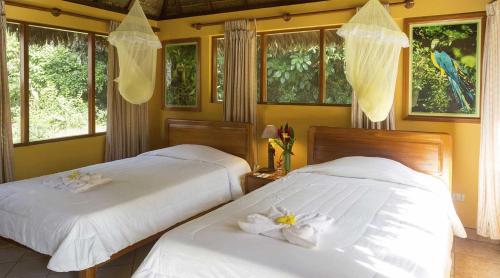 Dos camas en un dormitorio con sábanas blancas y flores. en Tambopata Ecolodge, en Tambopata