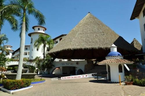 a building with a straw roof and a building with a tower at NEW Royal Pacific Condo 2 Pools Tennis Marina in Puerto Vallarta