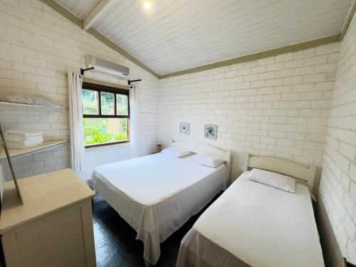 two beds in a small room with a window at Pousada North Shore Maresias - 2 quadras da praia - Casas de 2 quartos - 80 m2 -2 banheiros -piscina sauna - estacion-churrasq privativa -wifi animais de peq porte roupa de cama e banho in Maresias