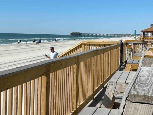 a man standing on a wooden boardwalk on the beach at Ocean Breeze Beachfront Condo, Newly Renovated in Myrtle Beach