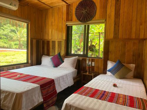 two beds in a room with wooden walls and windows at Quế Homestay in Hòa Bình