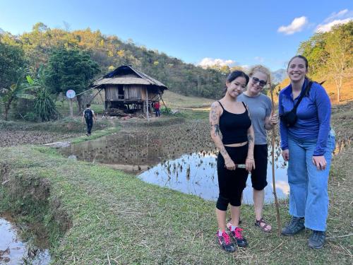 three women posing for a picture in front of a village at Quế Homestay in Hòa Bình
