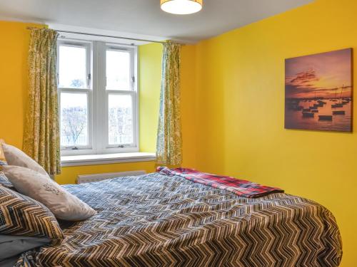 a bedroom with a bed with yellow walls and a window at Cowie Mill Apartment in Stonehaven