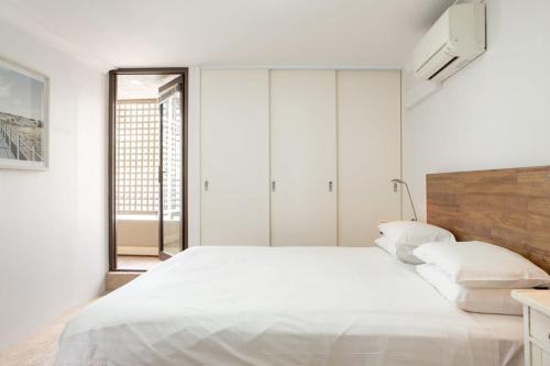een witte slaapkamer met een groot bed en een raam bij Beachfront Manly Apartment With Balcony & Parking in Sydney