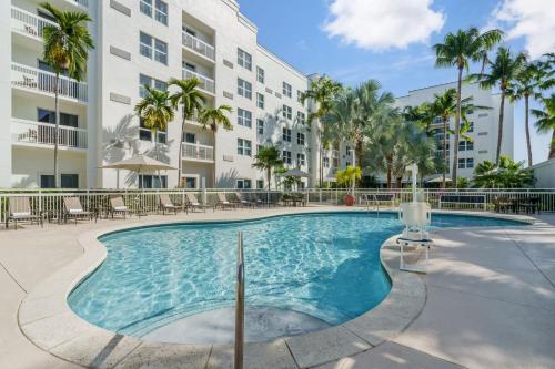 a pool with chairs and palm trees in front of a building at Courtyard by Marriott Miami Aventura Mall in Aventura
