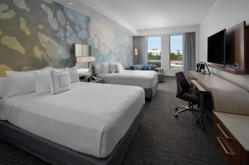 a hotel room with two beds and a desk at Courtyard by Marriott Delray Beach in Delray Beach