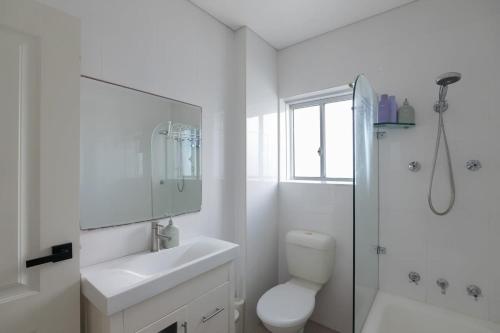 a white bathroom with a toilet sink and a shower at Stunning Maroubra Beachview Apt with Parking in Sydney