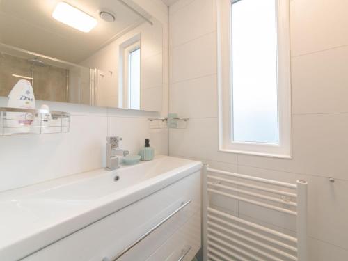 ein weißes Badezimmer mit einem Waschbecken und einem Spiegel in der Unterkunft Chalet with decorative fireplace on a holiday park in Wemeldinge