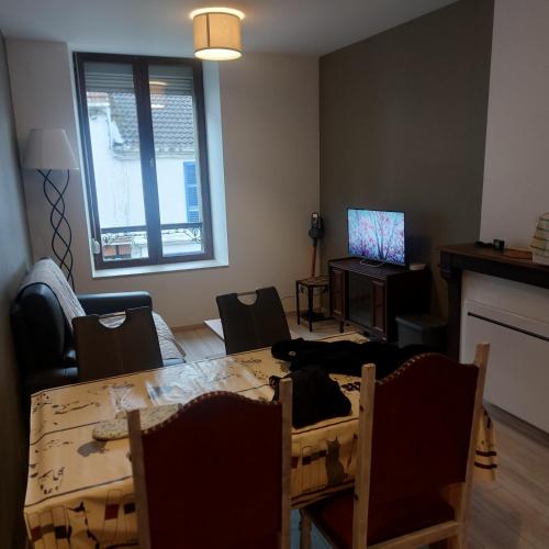 een woonkamer met een tafel en stoelen en een televisie bij Les hortensias in Bourbonne-les-Bains