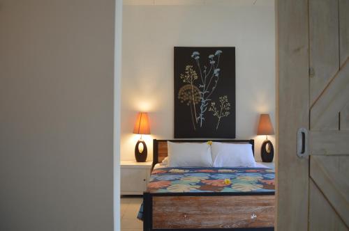 een slaapkamer met een bed met 2 lampen en een schilderij bij Little Pond Homestay in Sanur