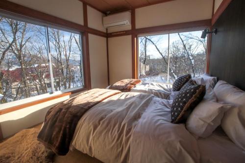 a large bed in a room with two windows at Lucky Duck Cabin Myoko in Myoko
