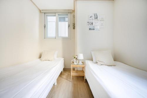 two beds in a white room with a window at Ehwa Blossom in Seoul