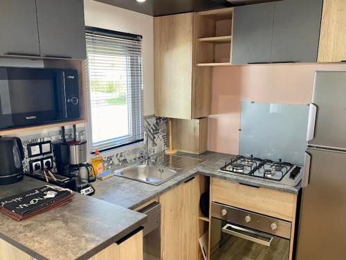 a kitchen with a stove and a refrigerator and a sink at Mobil-Home 3 Chambres, TOUT CONFORT, Option "DRAPS FOURNIS" Disponible ! in Pont-Aven