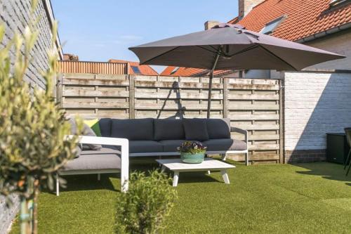 a blue couch and an umbrella on a lawn at Huswell - Summer-house with sunny garden nearby beach in Knokke-Heist