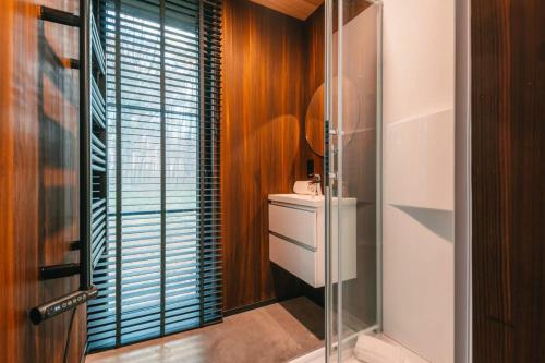 a bathroom with a glass shower and a sink at Cabin in the woods with hottub in Stekene