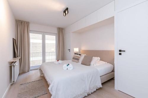 ein weißes Schlafzimmer mit einem großen Bett und einem Fenster in der Unterkunft Luxurious and modern family apartment with incredible view over the beach in Knokke-Heist