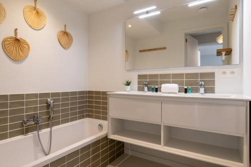een badkamer met een wastafel, een bad en een spiegel bij City at Sea - Modern 1 bedroom apartement in Oostende