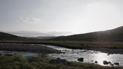 a river in the middle of a field with mountains at Gairnshiel lodge - Unique & exclusive lodge next to the castle in Ballater