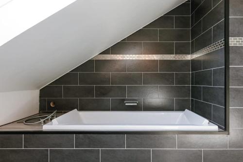 a white bath tub in a bathroom with black tiles at Spacious house with garden and parking in Blankenberge