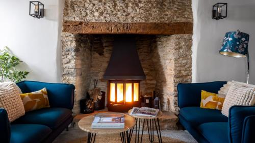 a living room with blue couches and a stone fireplace at Gable Cottage in Meysey Hampton