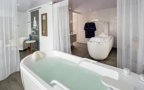 Baño blanco con bañera y lavamanos en Hôtel Château des Tourelles, Thalasso et piscine d'eau de mer chauffée en Pornichet