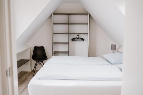 ein Schlafzimmer mit einem weißen Bett und einem schwarzen Stuhl in der Unterkunft Ons Kotje in Aagtekerke