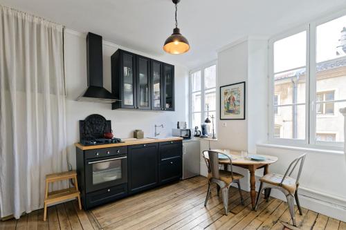 une cuisine avec des armoires noires, une table et des chaises dans l'établissement Le Boudoir de Stanislas - Appt au cœur de Nancy, à Nancy
