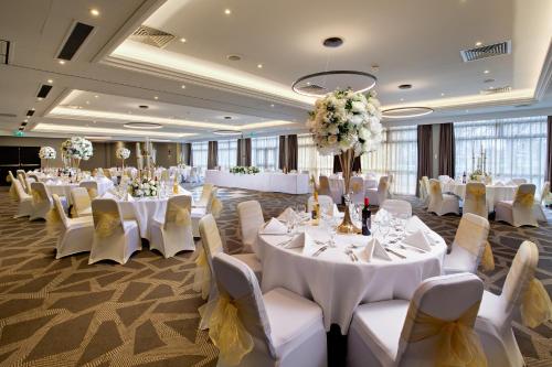 Un salón de banquetes con mesas y sillas blancas y flores. en DoubleTree by Hilton London Ealing, en Londres