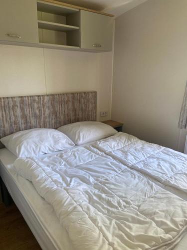een ongeëvenaard bed in een slaapkamer met witte lakens bij Camping de Duinhoeve Chalet Vogel not for companies in Nieuw-Haamstede