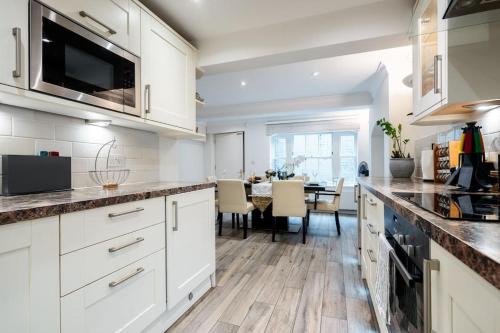 a kitchen with white cabinets and a dining room at Spacious, Bright & Cosy ~ Ideal Victoria Location! in London